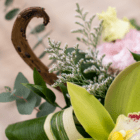 Elegant floral arrangement with green leaves, yellow orchid, pink rose, and curly wood accent.