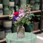 Vibrant bouquet in decorative vase on ornate green table, surrounded by potted plants.