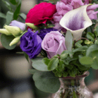Close-up of a colorful bouquet featuring purple roses and greenery in a decorative vase.