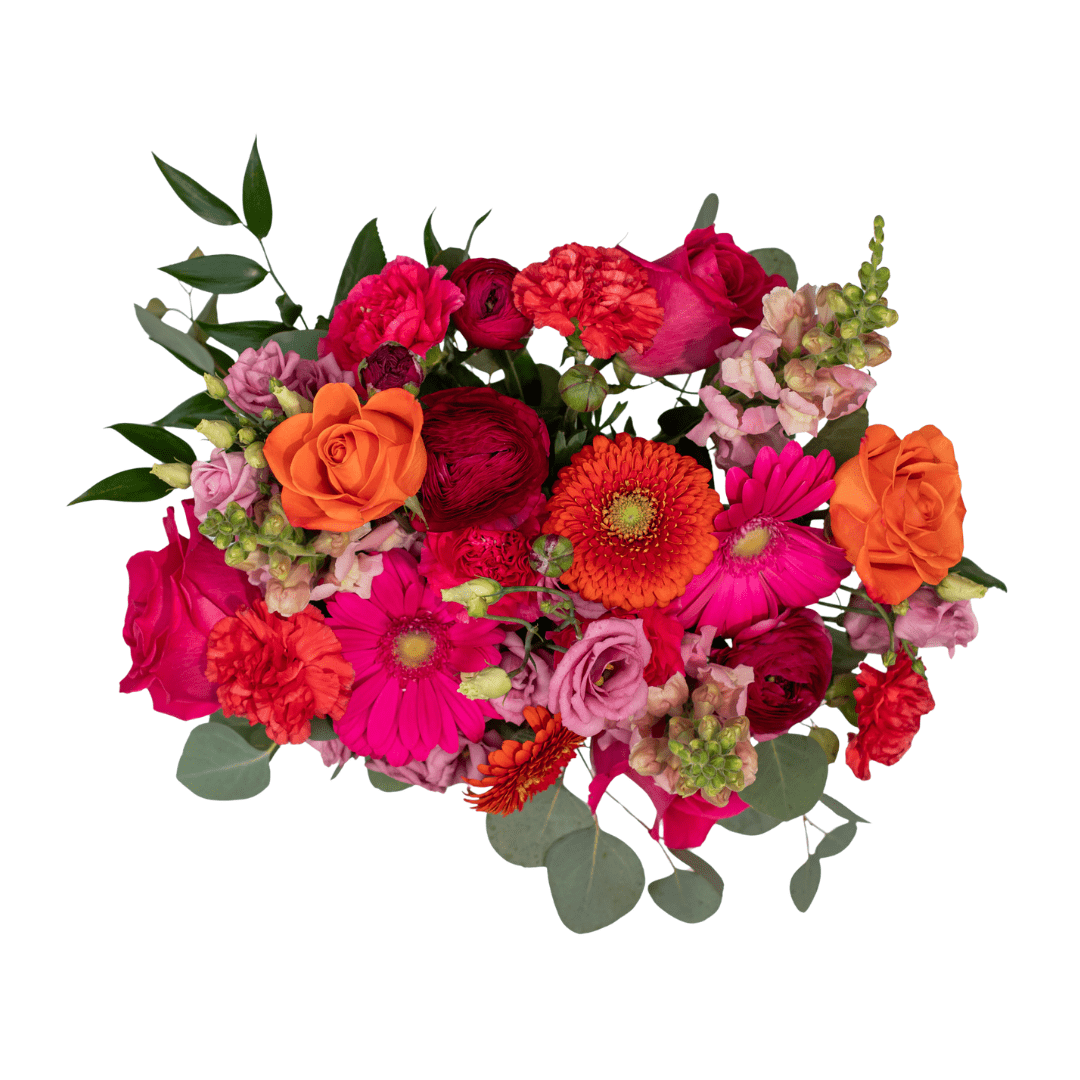 A view from above of a fresh floral arrangement in a pink ceramic jug with bold pink and orange cut flowers, like gerberas, roses, snapdragons, carnations, and lisianthus.