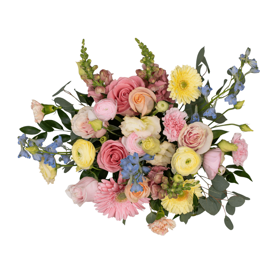 A view from above of a fresh floral arrangement in a pink ceramic jug with light pink, yellow, peach, and blue-coloured flowers, like gerberas, roses, delphinium, carnations, and snapdragons.