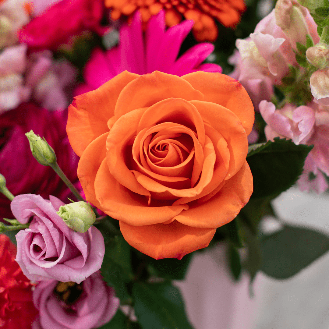 A close-up of a bold orange rose in a fresh floral arrangement!