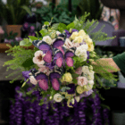 A fresh floral bouquet with pale pink and yellow lisianthus, as well as white and purple, with eucalyptus and other greenery accents, and faux purple butterflies floating over the foliage and blooms.
