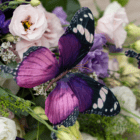 A close-up of a faux purple butterfly in a fresh floral arrangement.