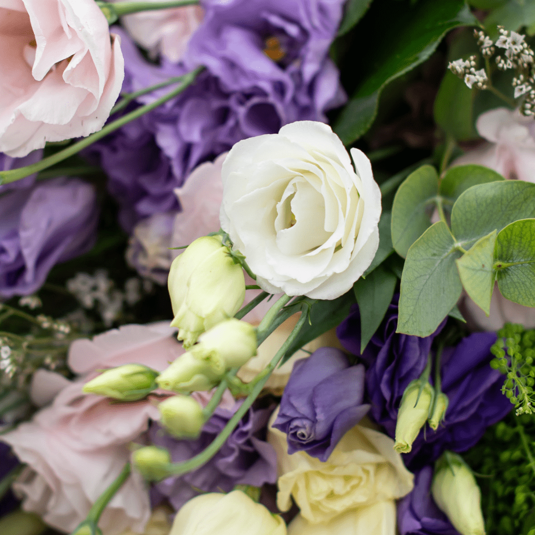 A close-up of white lisianthus blooms in a fresh floral arrangement with other pale pink and purple flowers.