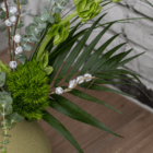 A close-up of a dark green palm leaf in a floral arrangement with other stems of greenery.