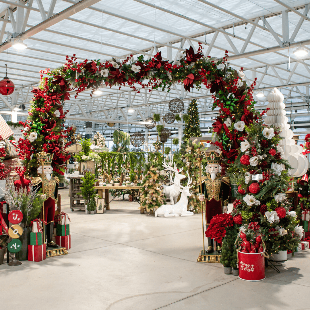 A traditional red, green, and white Christmas display in a greenhouse with a large arch with artificial greenery and two life-size nutcrackers below in the same colour palette.