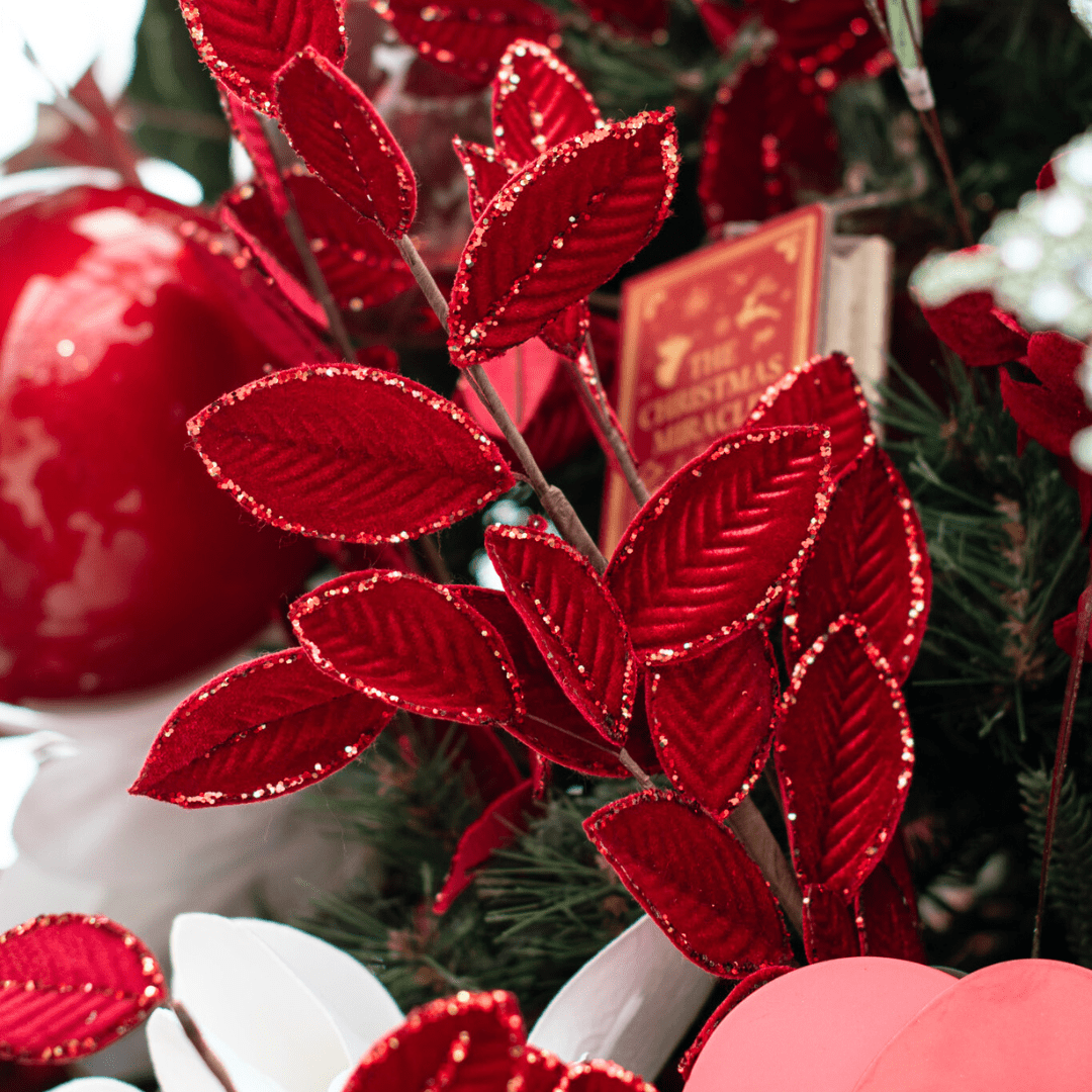 Faux red velvety leaf pick in an artificial green Christmas tree with other red and white decor.