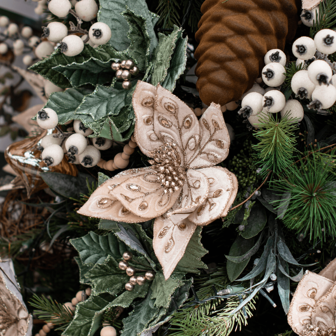 A faux beige and gold poinsettia pick in an artificial green Christmas tree with other white, brown, and sage decorations.
