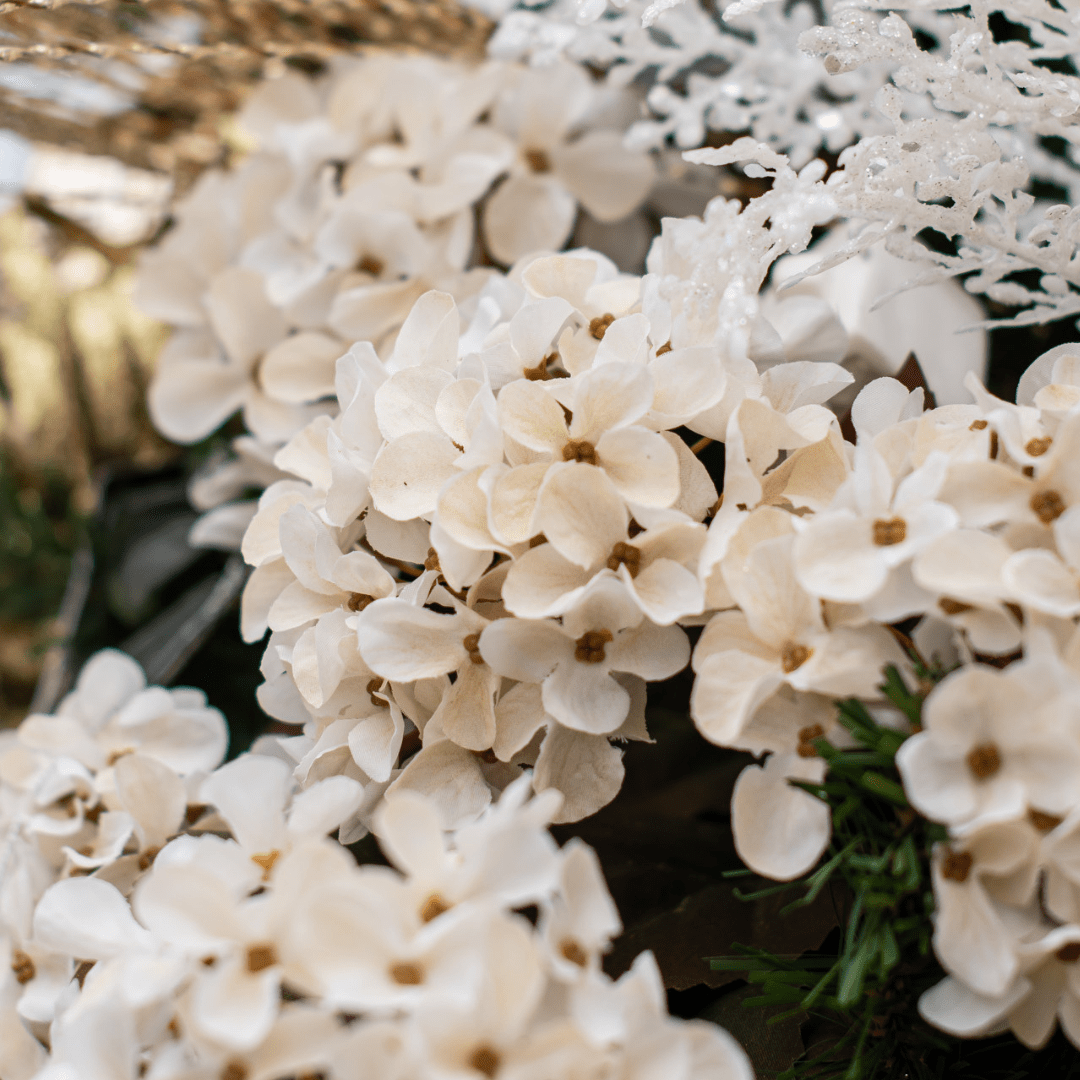 A fluffy faux cream-coloured hydrangea pick in an artificial green Christmas tree.