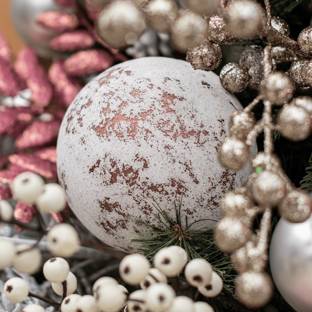 A large round white ornament with pinky bronze splotches in an artificial green Christmas tree surrounded by other sparkly pink and gold picks.