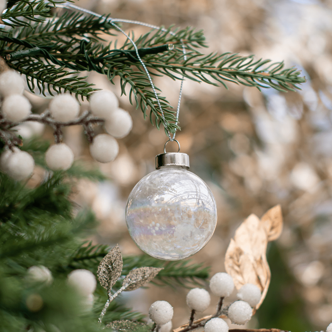 A round white/opaque ornament hangs from a green artificial Christmas tree branch.