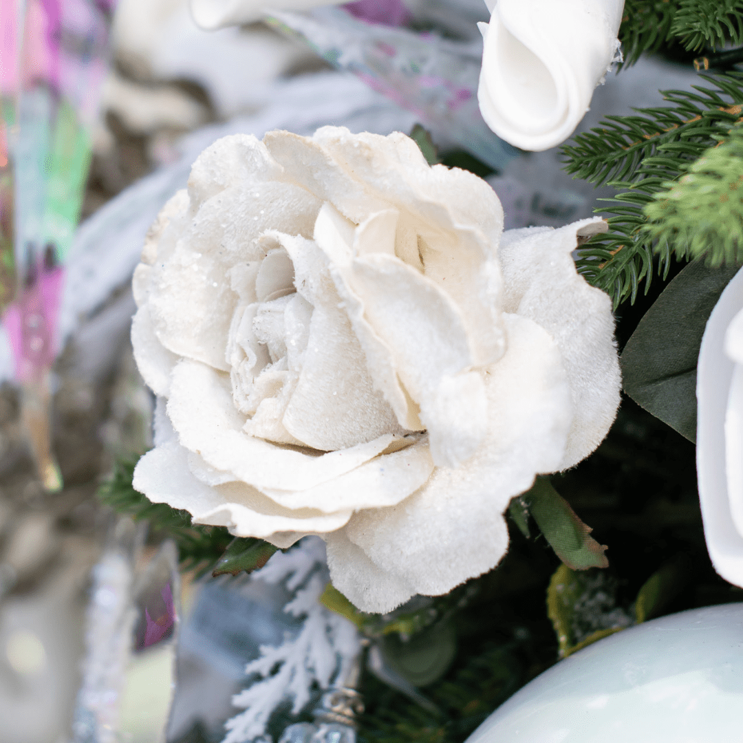A close-up of a faux white sparkly/frosted rose pick in a green artificial Christmas tree.