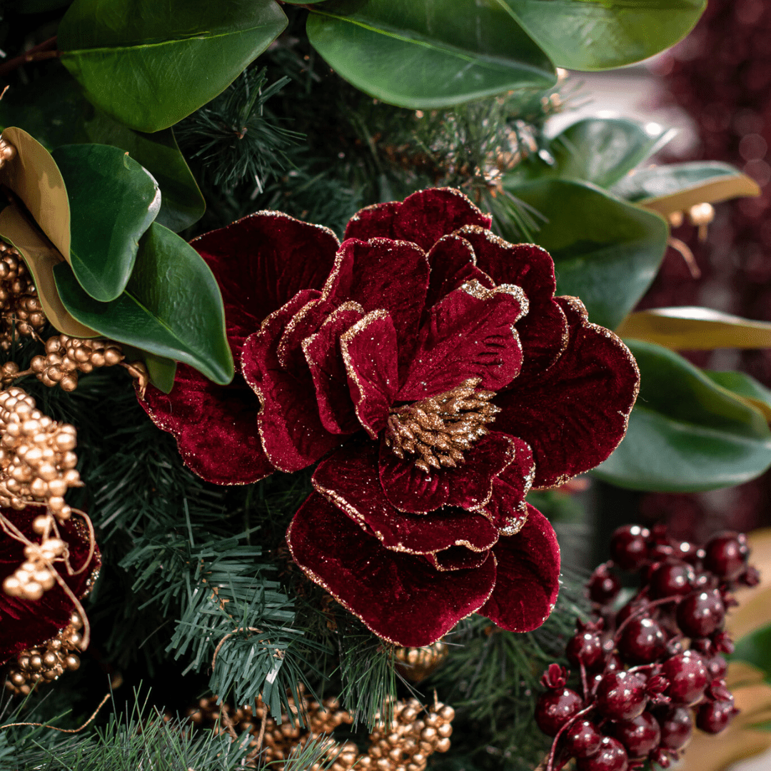 A faux burgundy and gold poinsettia pick in an artificial green Christmas tree.