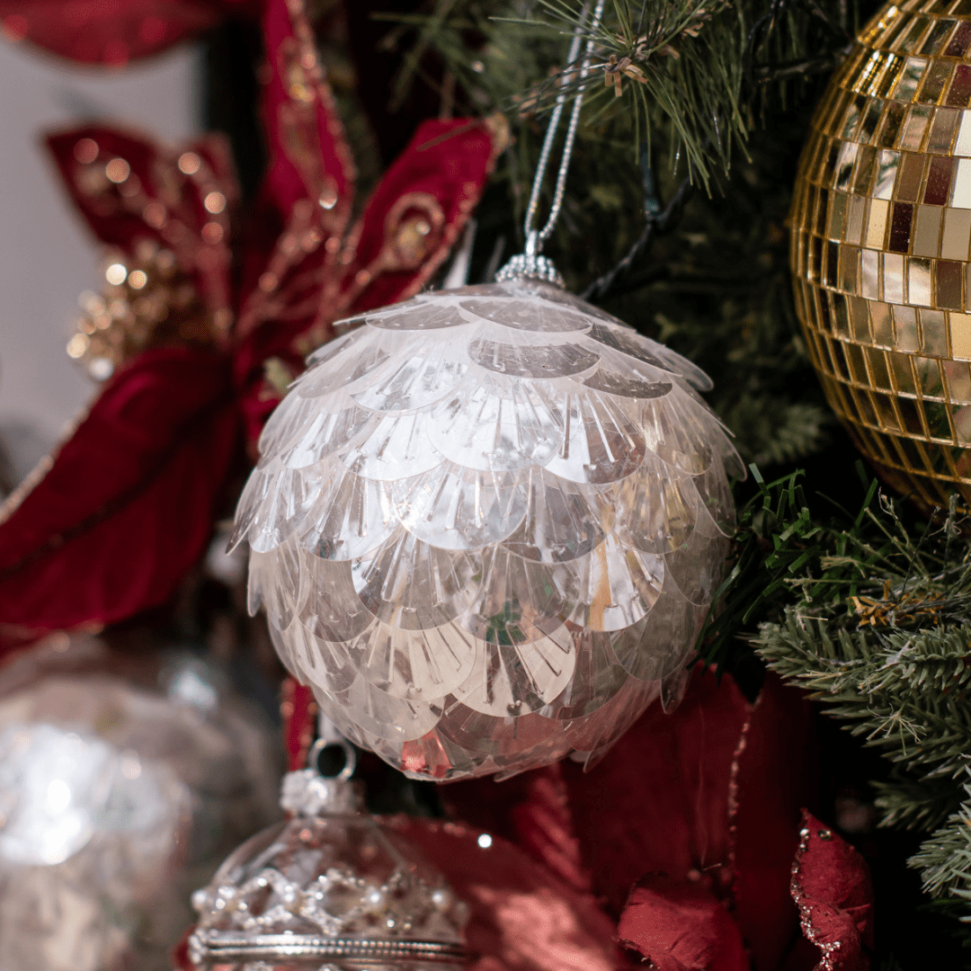 A round plastic white/iridescent ornament with a scalloped design hanging in an artificial green Christmas tree.
