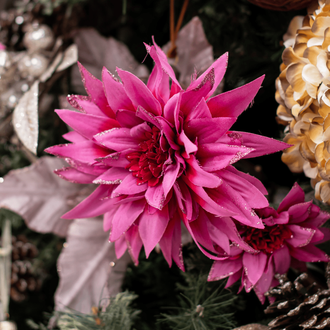 A bright pink dahlia flower pick in an artificial green Christmas tree.