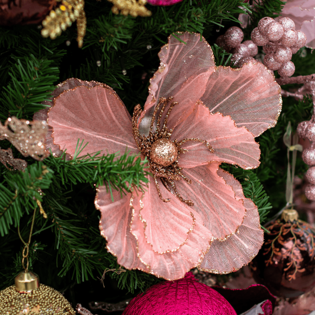 A pink and bronze glittery decorative poinsettia pick in an artificial green Christmas tree.