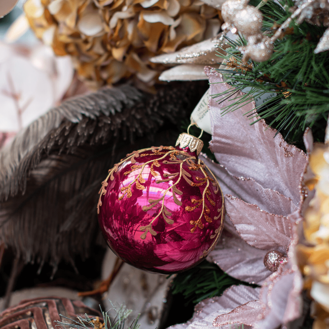 A reflective pink and bronze circular ornament hangs from an artificial Christmas tree decorated with more pink and browns.