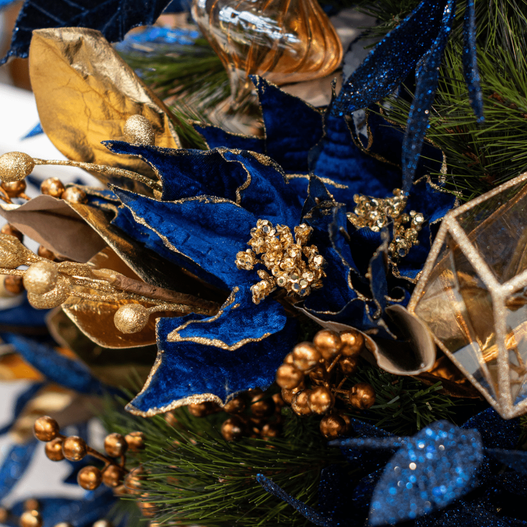 A faux dark blue and gold velvety poinsettia pick in an artificial green Christmas tree.