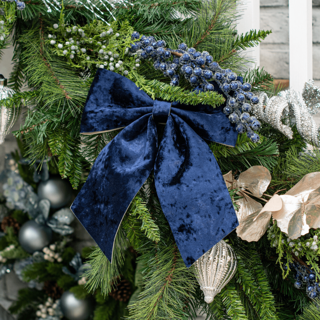 A blue velvety bow in an artificial garland hanging on a staircase.