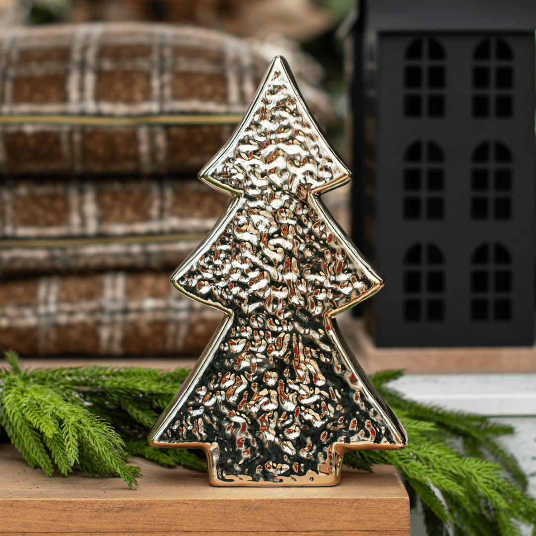 A gold decorative Christmas tree sits on a wooden mantel with artificial greenery behind it.