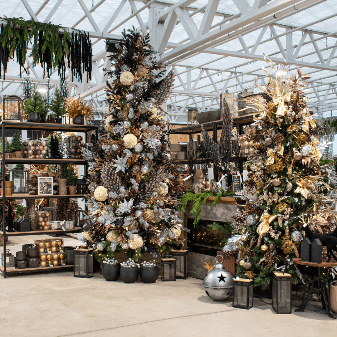 A gold, black, silver, and champagne-coloured Christmas display in a greenhouse with artificial Christmas trees, a stone fireplace, etc.