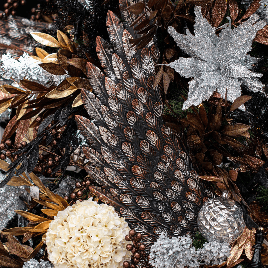 A metal silver, bronze, and black angel wing is displayed in an artificial Christmas tree with other silver, brown, and gold accents.