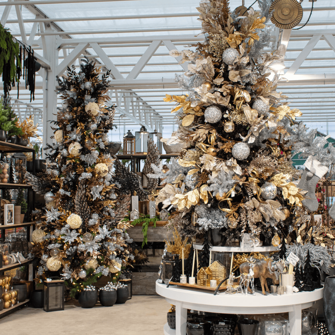 A gold, black, silver, and champagne-coloured Christmas display in a greenhouse with artificial Christmas trees, a stone fireplace, etc.