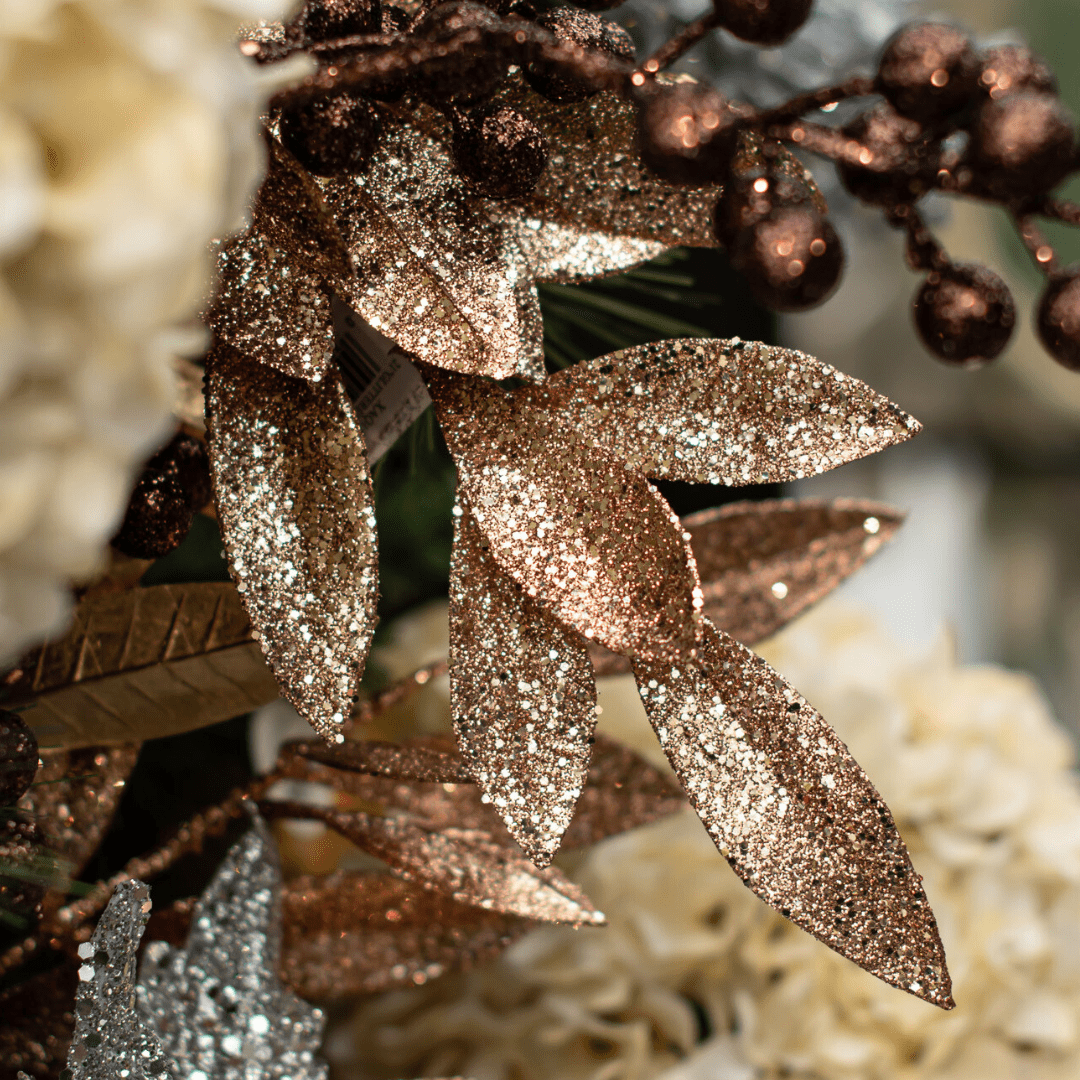 A champagne-coloured sparkly leaf pick surrounded by other similar picks in brown tones in an artificial green Christmas tree.
