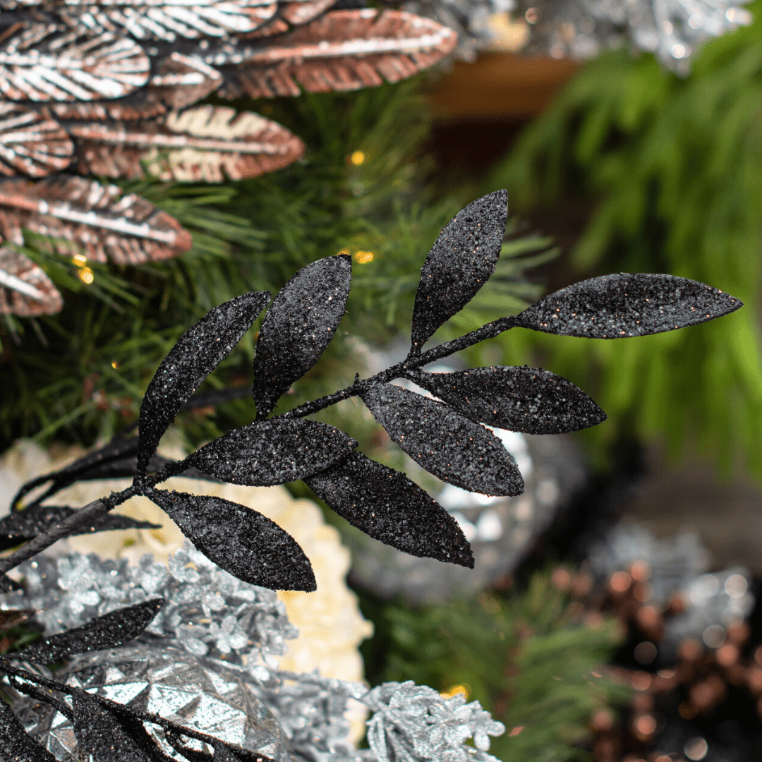 A black sparkly decorative leaf pick in an artificial green Christmas tree.
