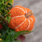 A close-up of an orange pumpkin pick made of twine in an indoor mixed planter.