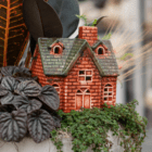 A close-up of an orange and brown brick-style ceramic house in a fall-themed indoor mixed planter.