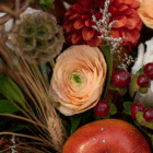 A close-up of a peach ranunculus in a fall floral arrangement.