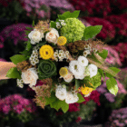 An above view of a white, yellow, and green floral bouquet with roses, carnations, lisianthus, wax flower, strawflower, hydrangea, etc.