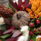 A close-up of a decorative brown burlap pumpkin pick in a fall floral arrangement.