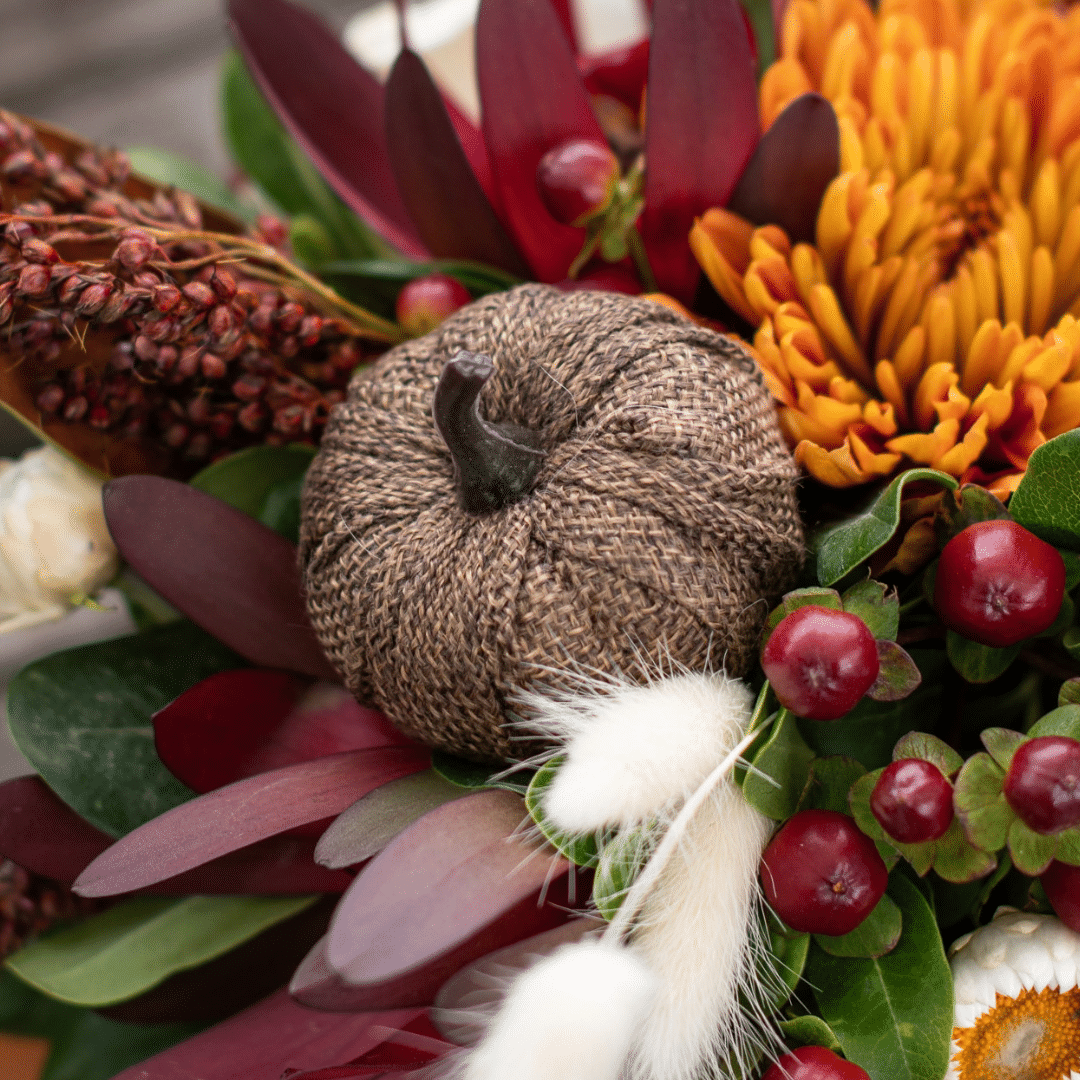 A close-up of a decorative brown burlap pumpkin pick in a fall floral arrangement.