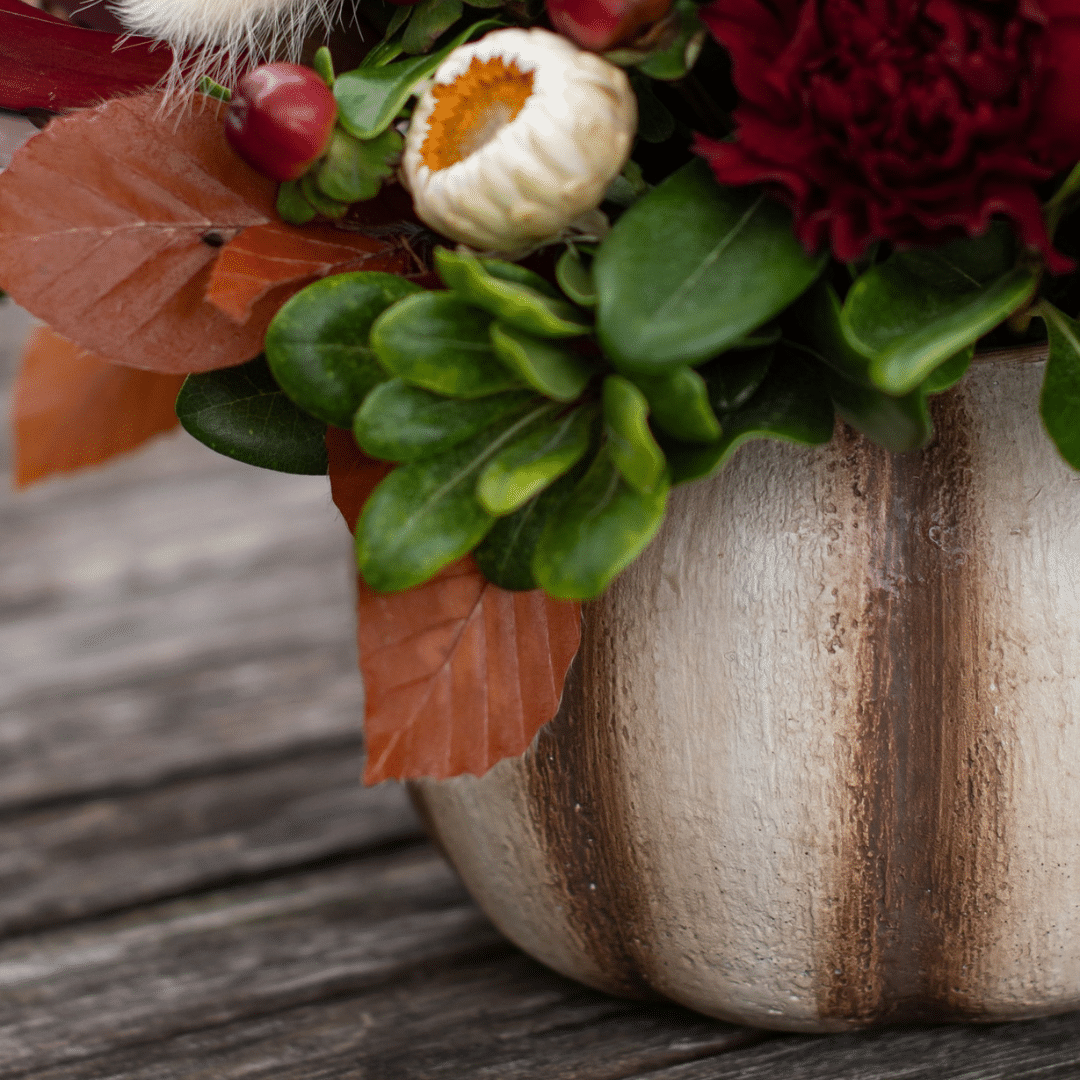 A close-up of a cream and brown striped ceramic pumpkin pot as part of a fall floral arrangement.