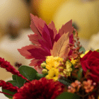 A close-up of a wooden orange-red-yellow leaf pick in a fall floral arrangement.