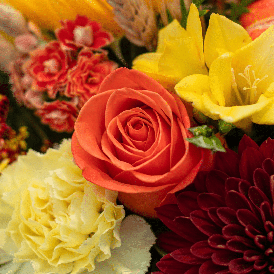 A close-up of an orange rose in a fall floral arrangement.
