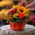 A floral arrangement in an orange ceramic pumpkin with sunflowers, yellow freesia, orange roses, etc.
