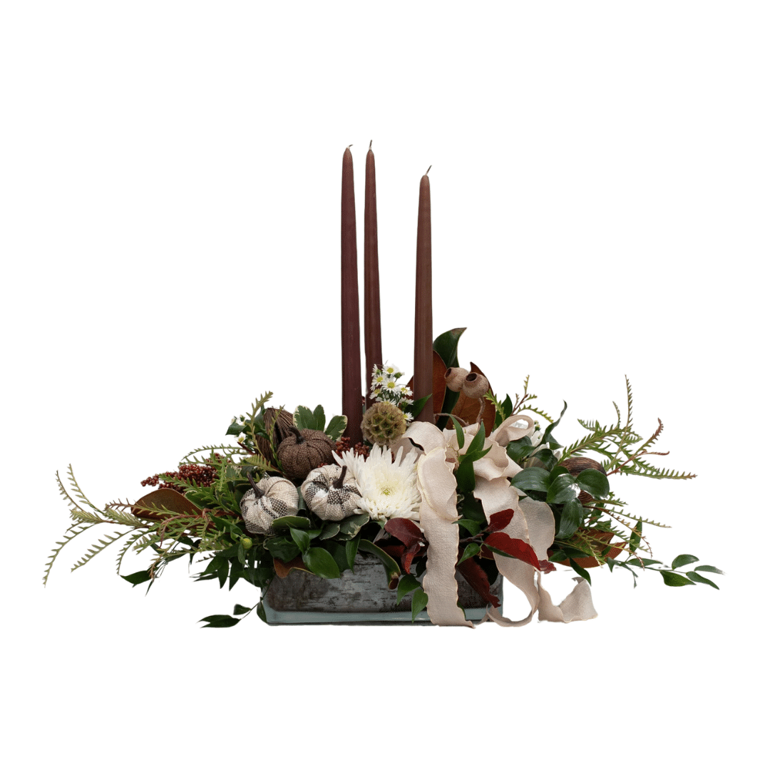 454 A fall floral arrangement with three brown taper candles, white mums, a cream-coloured ribbon bow, and other natural elements.