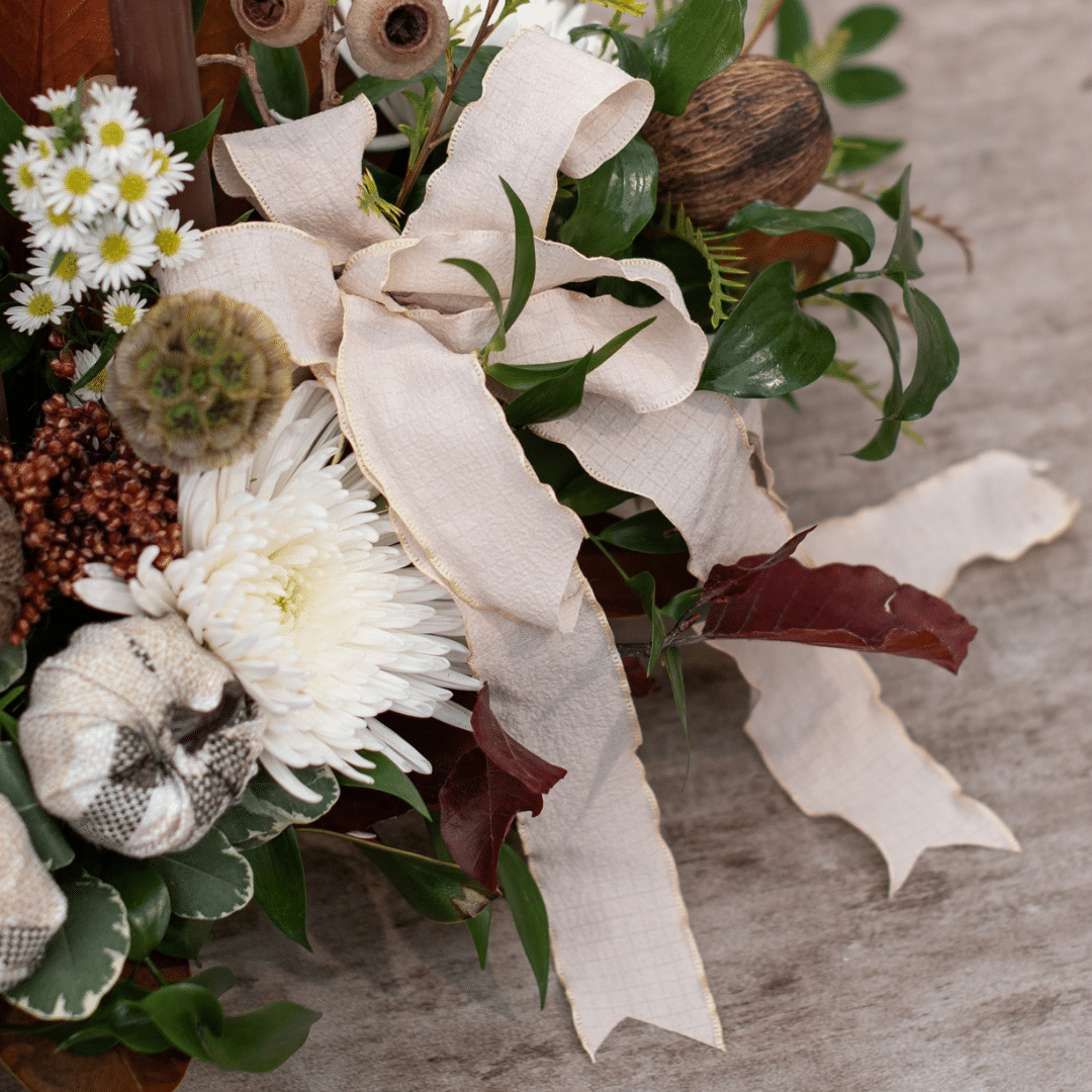 A close-up of an ivory ribbon bow in a fall candle floral centerpiece.