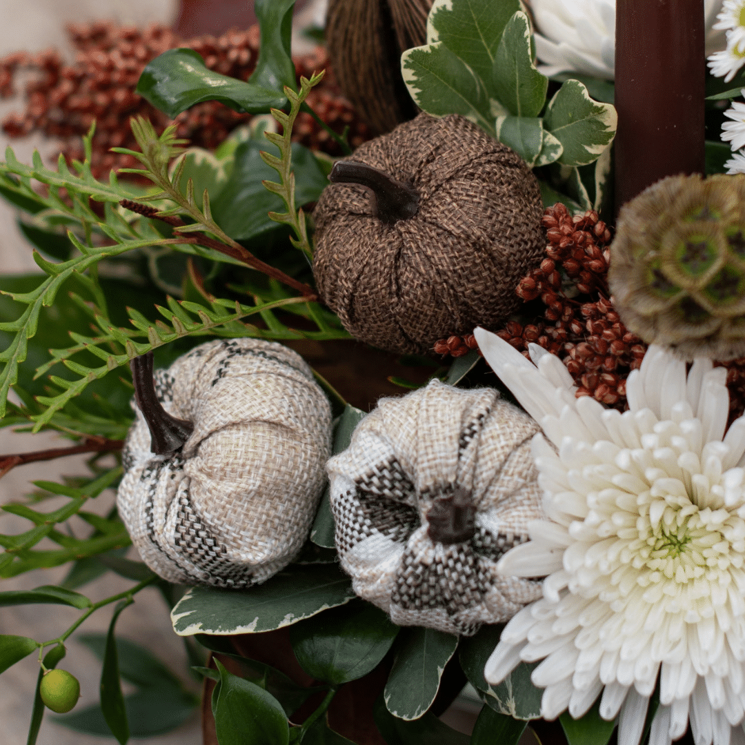 A close-up of a trio of decorative pumpkin picks made of brown and cream plaid burlap in a fall floral arrangement.