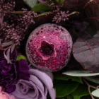 A close-up of a sparkly, fuchsia pomegranate in a berry-toned bouquet.