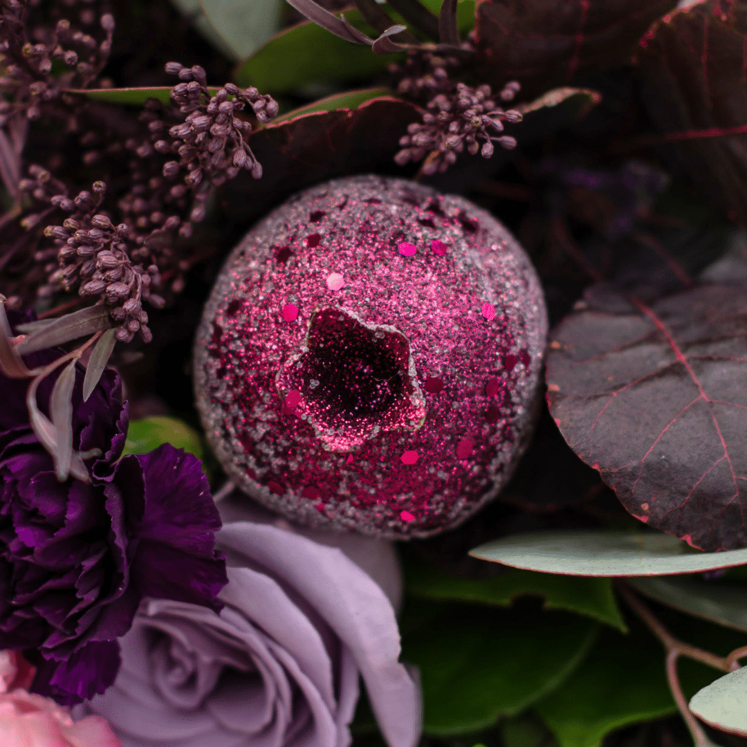A close-up of a sparkly, fuchsia pomegranate in a berry-toned bouquet.