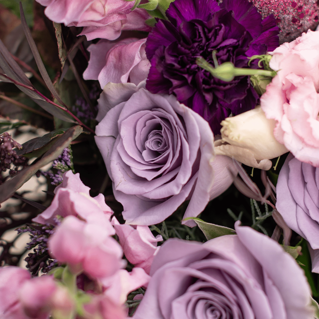 A close-up of a lilac rose in a berry-toned bouquet.