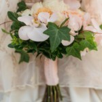 Elegant bridal bouquet with roses, orchids, and ivy leaves against lace fabric background. Perfect for weddings.
