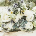 Elegant floral arrangement with white roses, succulents, and greenery on a wooden surface, perfect for weddings.