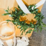 Green wreath with white ribbon on wooden chair, candle in glass holder, and scattered petals on carpet.