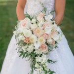 Bride holding elegant bouquet of roses and lilies in white gown, outdoors.